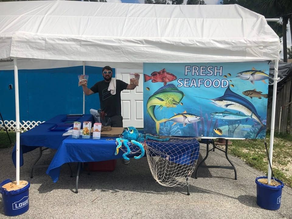Capt. J's seafood stand with a white tent, blue-draped tables and a colorful Fresh Seafood banner